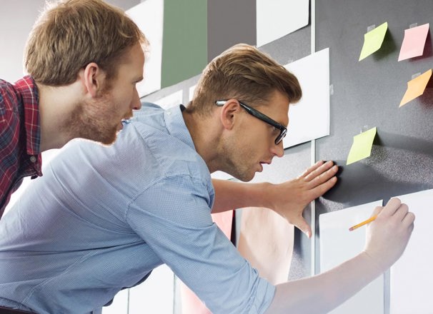 2 people writing on pieces of paper stuck  to the wall