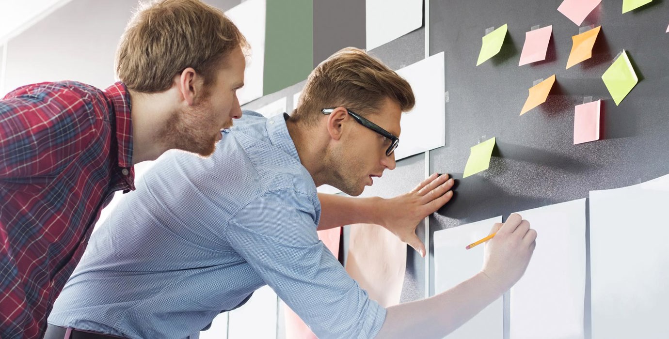 2 people writing on pieces of paper stuck  to the wall