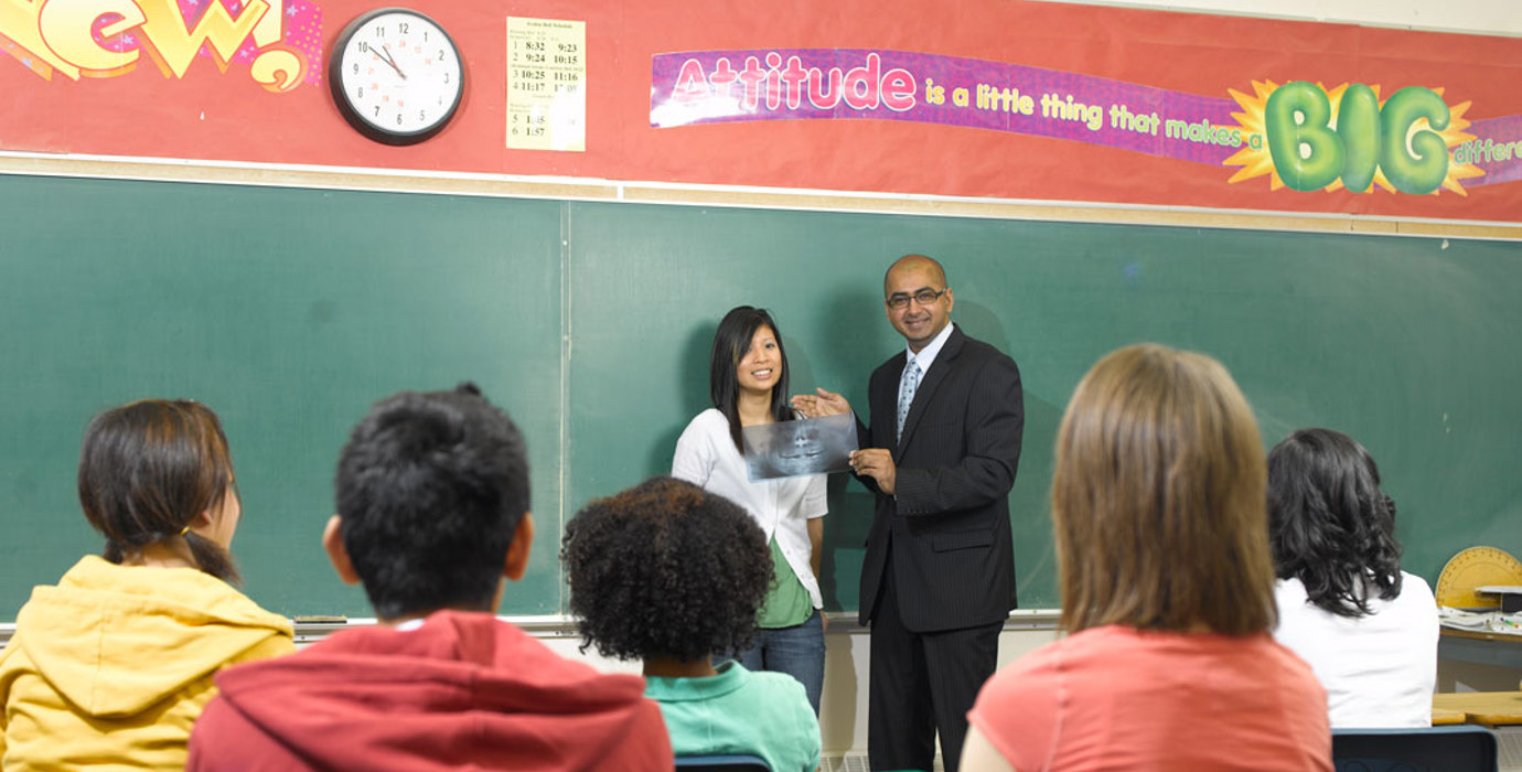 2 teachers standing in front of a classroom of youth