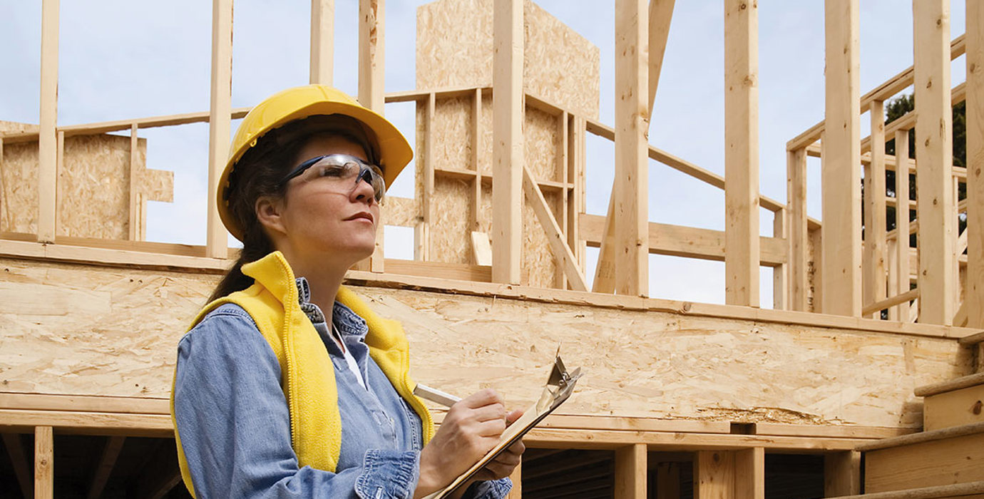 Person wearing a hard hat and safety glasses writing on a clipboard in a construction zone