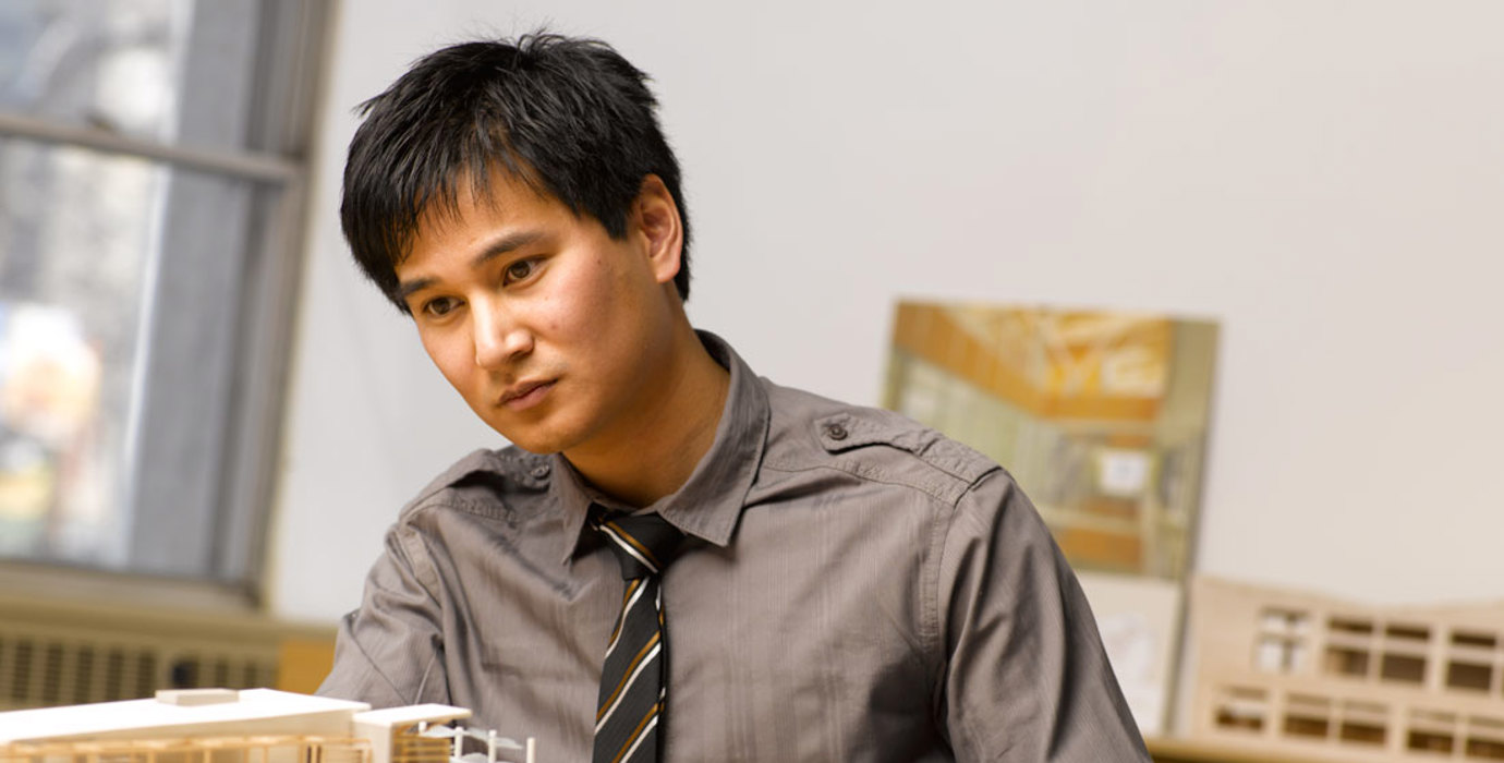 Architect in an office looking at a wooden model of a building