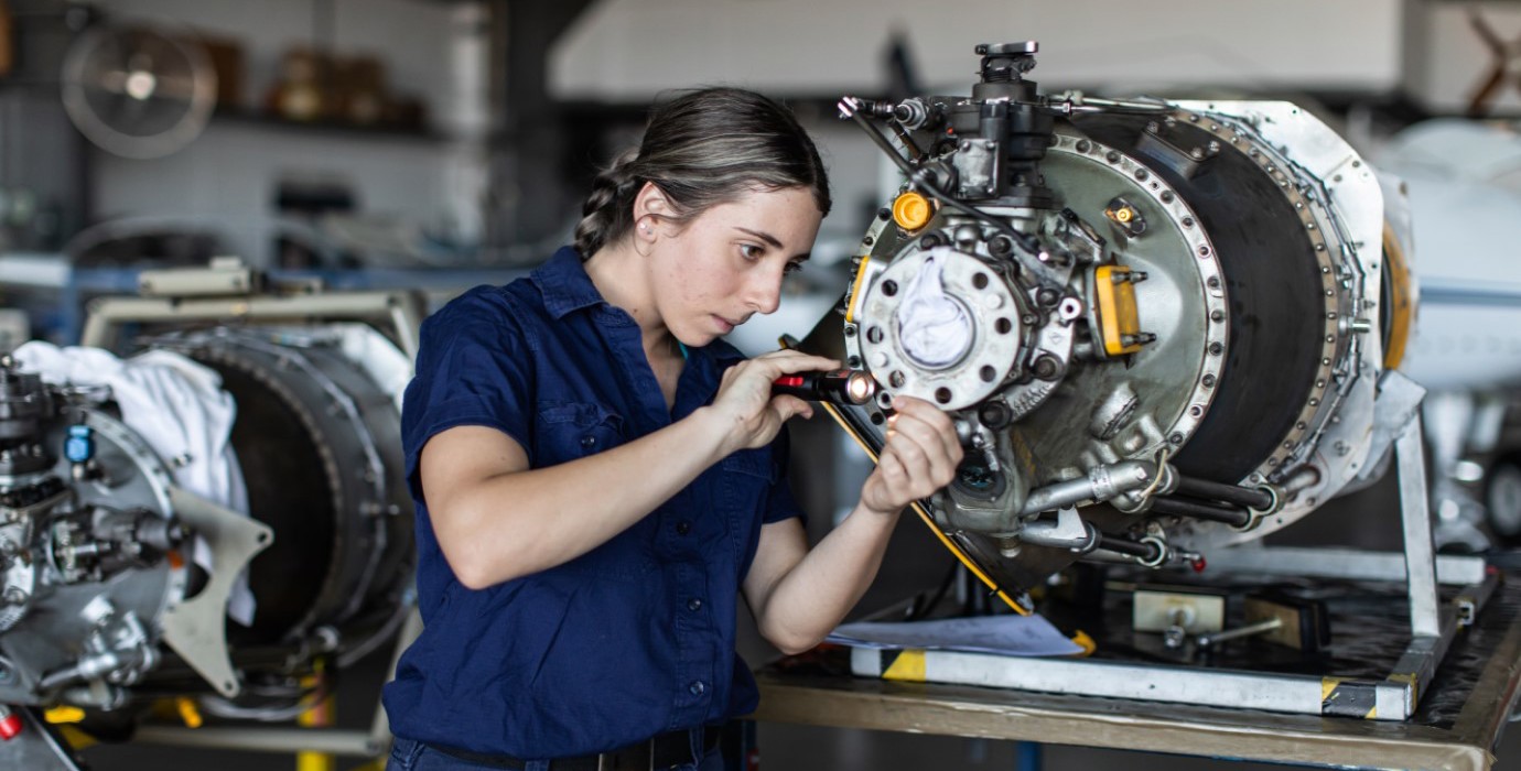 Apprentice aircraft engineer inspects parts in factory.
