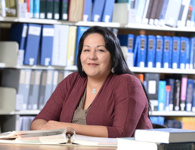 Person in a library sitting at a desk in front of bookshelves