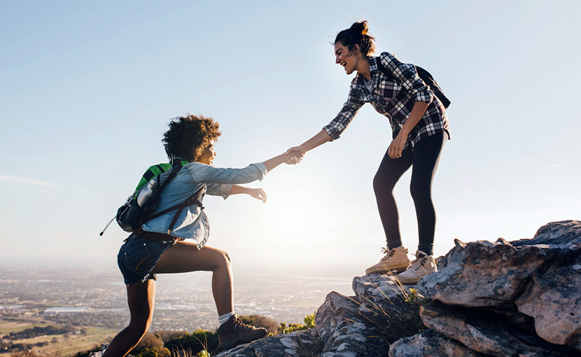 Friends helping each other climb up a hill