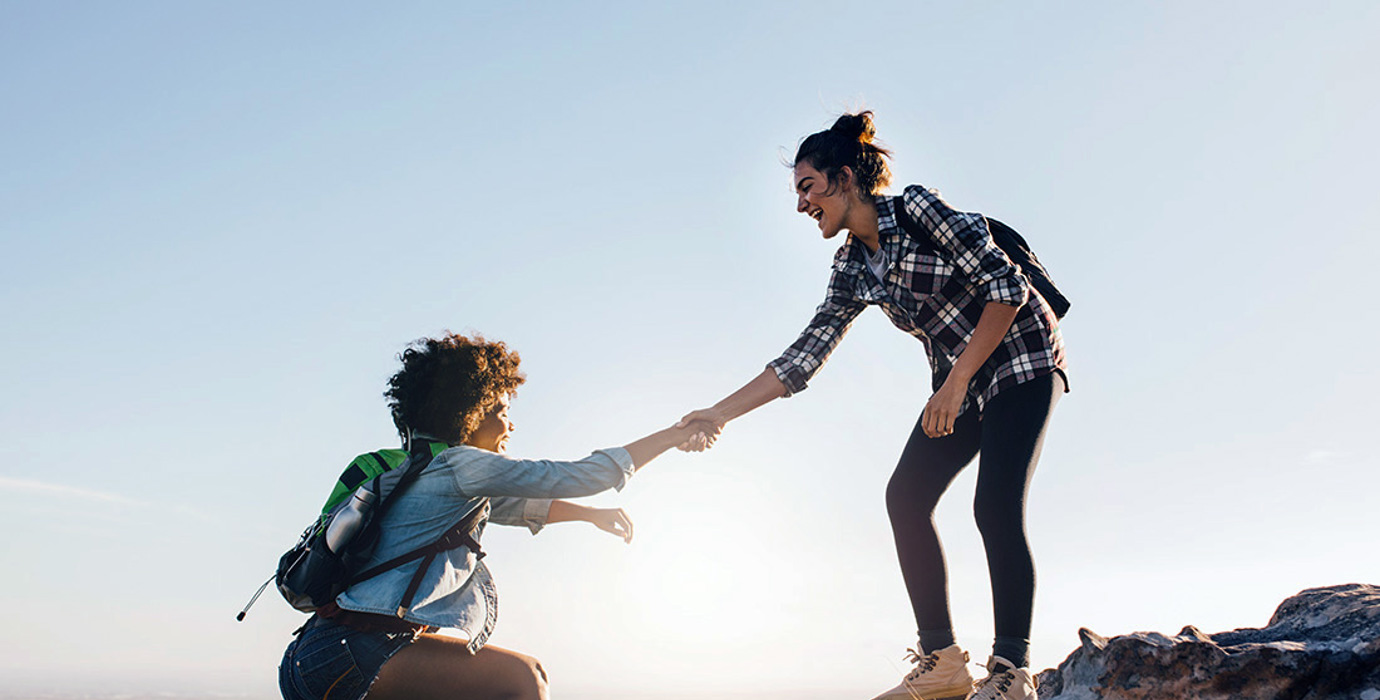 Friends helping each other climb up a hill