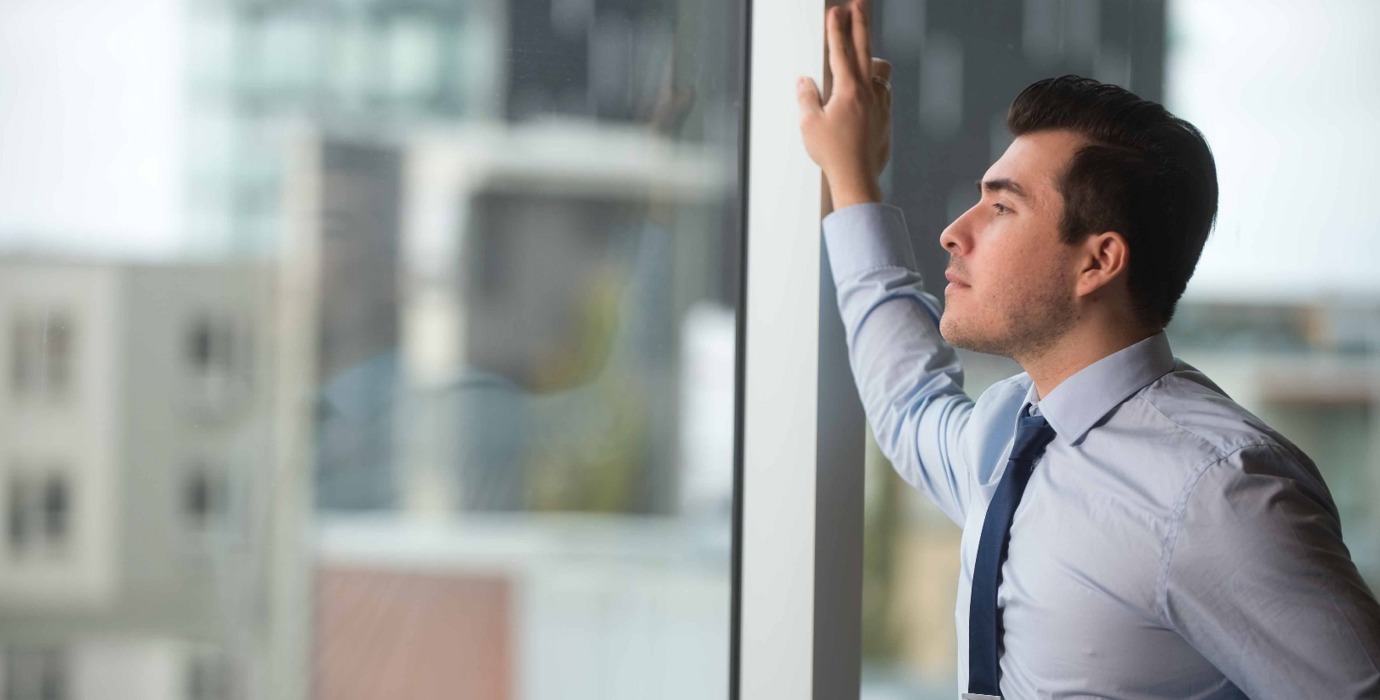 Person wearing business attire holding a mug and looking out a large window
