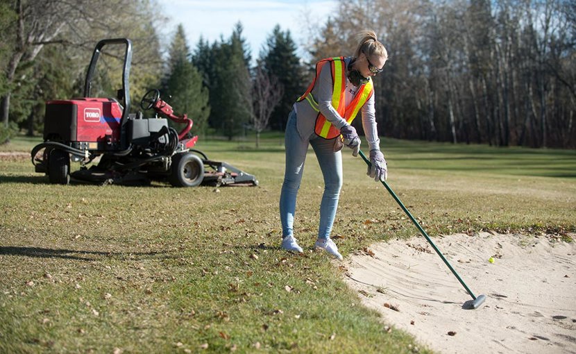 Golf course groundskeeper working on a sand bunker