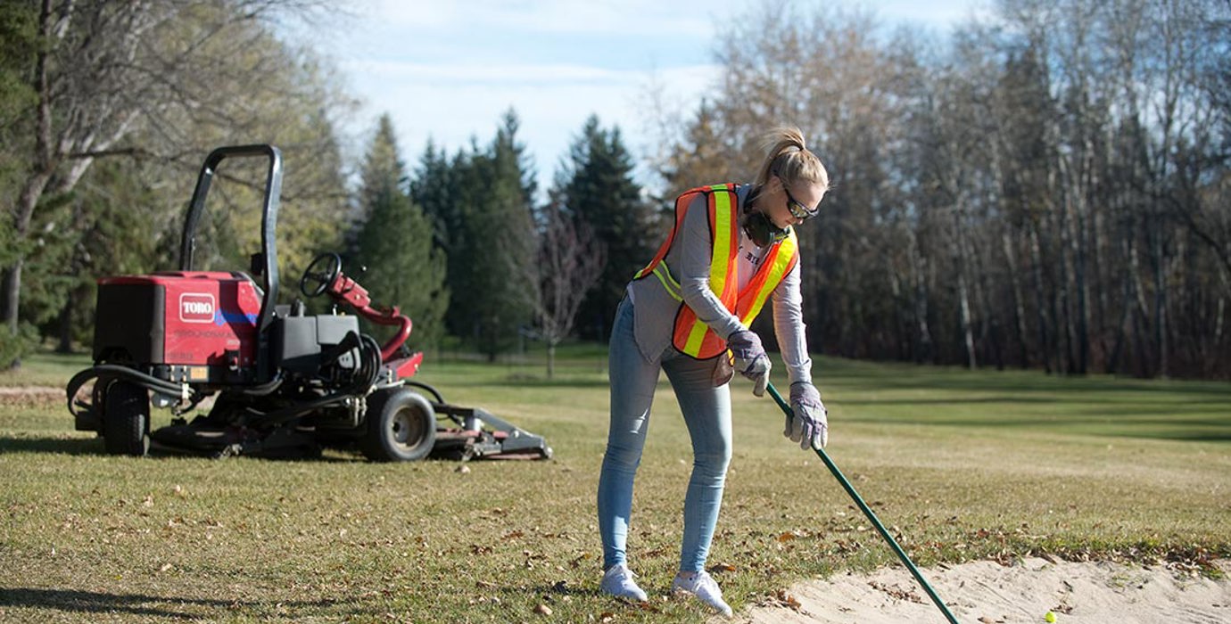 Golf course groundskeeper working on a sand bunker