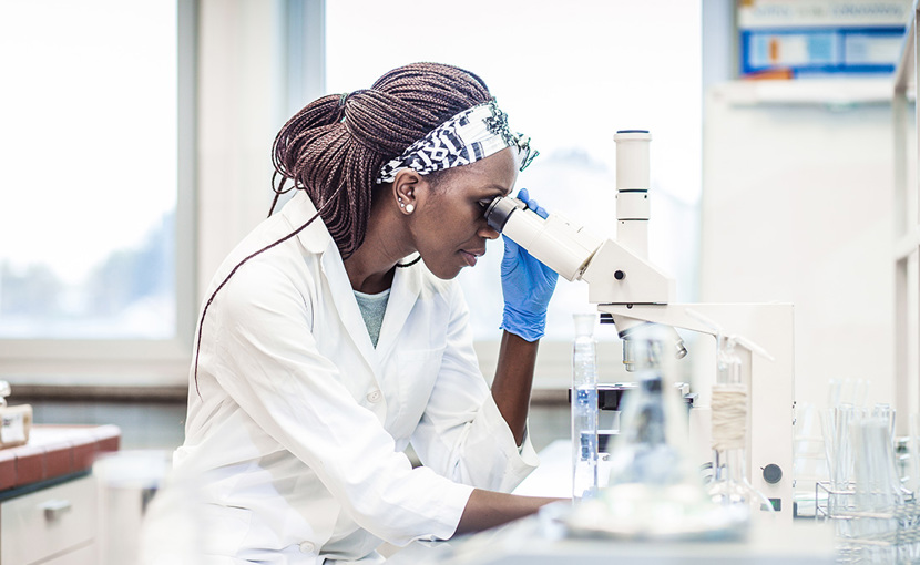 Scientist wearing a lab coat looking into a microscope in a laboratory