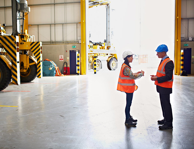 Employee and manager wearing hard hats discussing in a warehouse