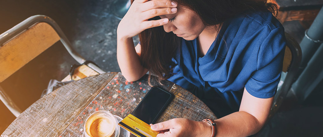 Person having a coffee with head in hand unhappily holding a credit card