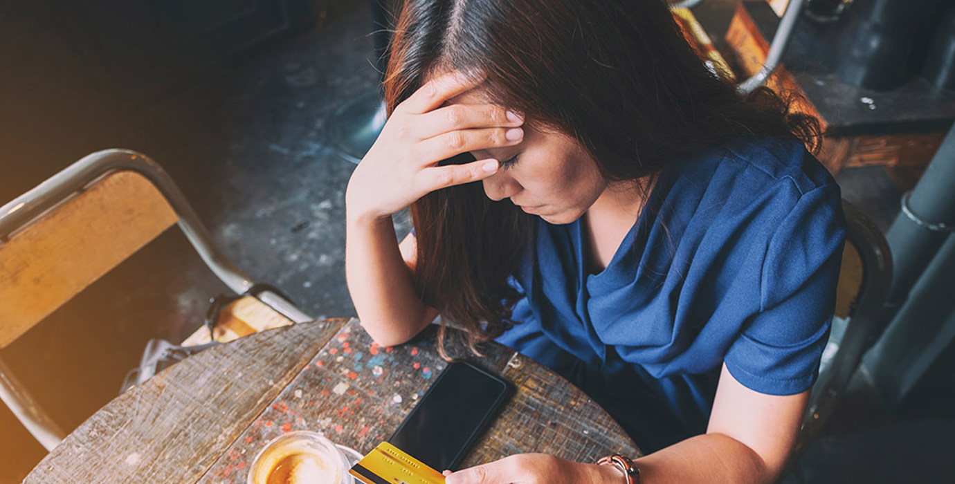 Person having a coffee with head in hand unhappily holding a credit card