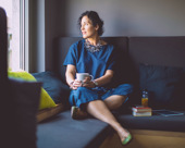 Person sitting on a couch looking out the window while holding a mug