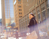 Person carrying a messenger bag and smiling while walking in a downtown area