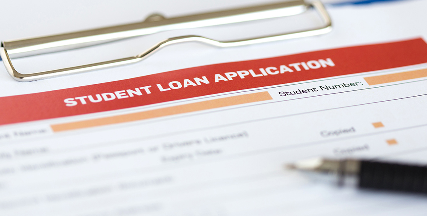 Paper application for student loan on a clipboard with a pen lying on top