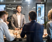 Person in a boardroom standing in front of 3 others during a meeting