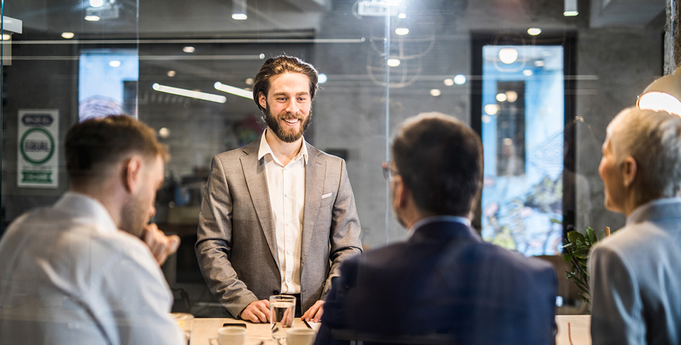 Person in a boardroom standing in front of 3 others during a meeting