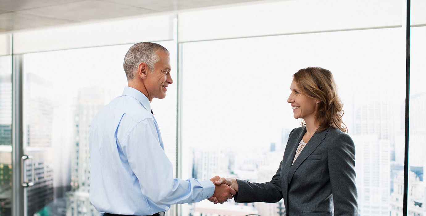 2 people in a boardroom shaking hands and smiling