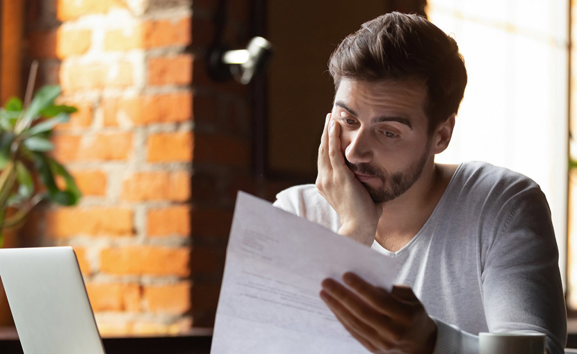 Worried person with chin in his hand reading a document in his other hand