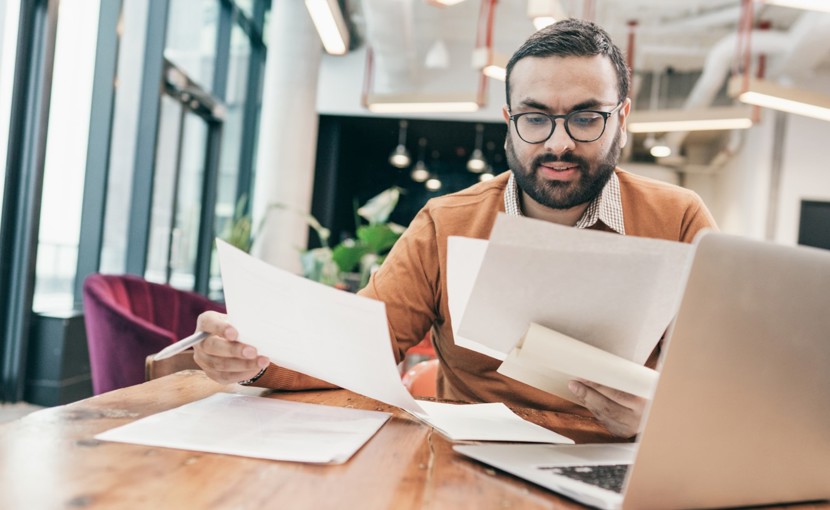 Person sitting at computer and looking through several pieces of paper.