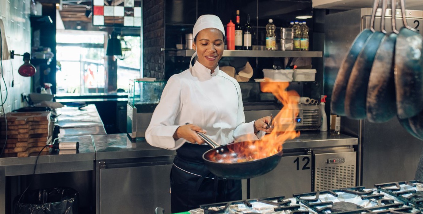 Female chef sauteing in a commercial kitchen.