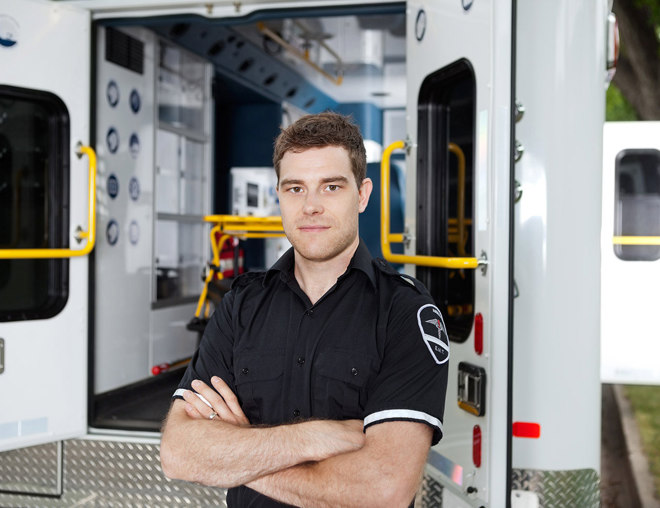 Male EMT with arms crossed standing outside of an ambulance.