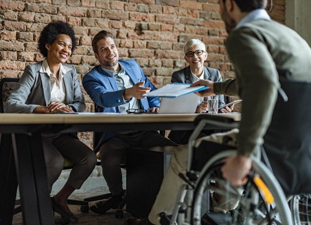Man in wheelchair hands his resume to human resources team before a job interview.
