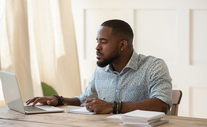 Man working on computer at desk with papers stacked beside him.