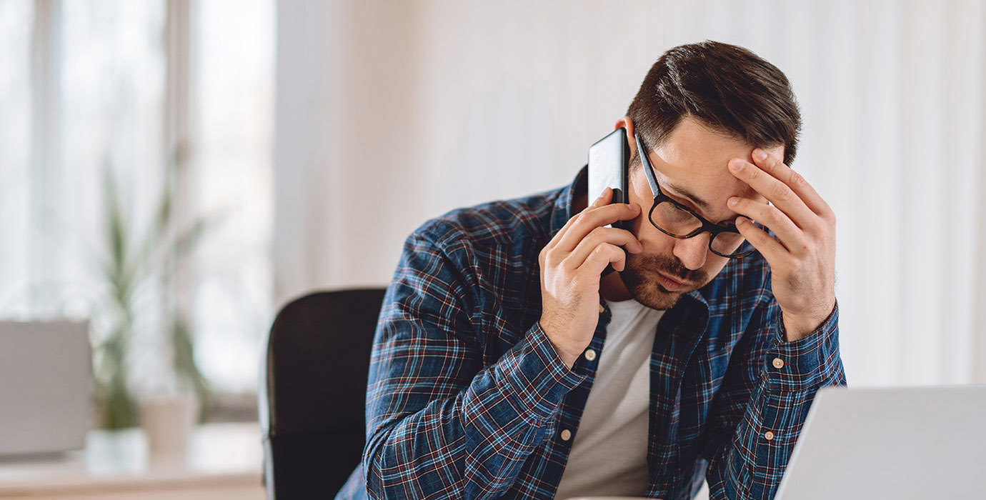 Worried man talking on phone while using laptop.
