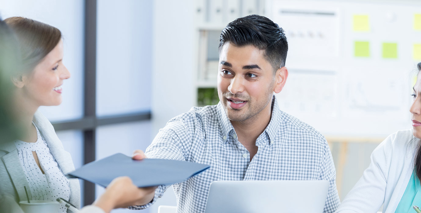 Business person passing a folder to a coworker during a meeting.