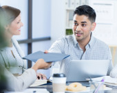 Business person passing a folder to a coworker during a meeting.