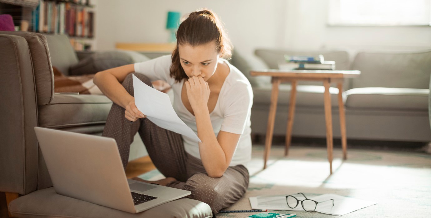 Woman sitting on floor while looking at papers and laptop.