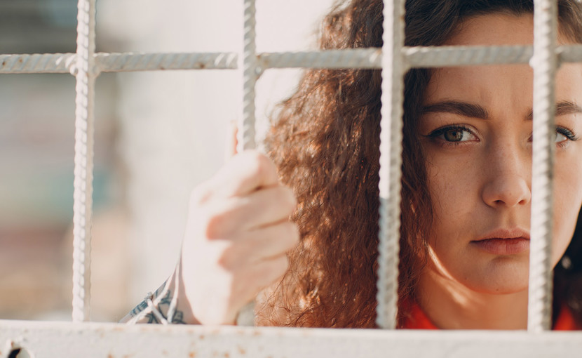 A person looking through bars and holding onto the barrier.