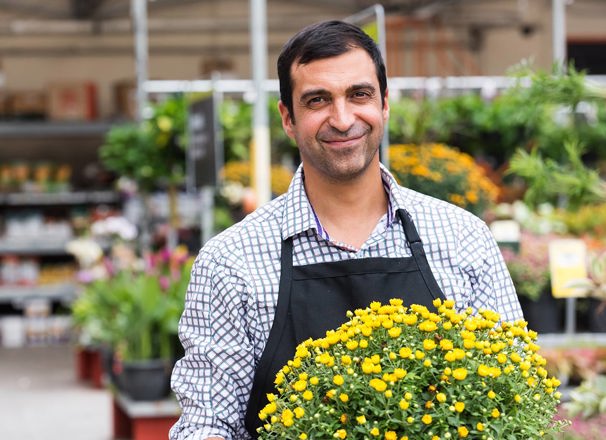 A smiling worker carries a potted plant in a garden centre.