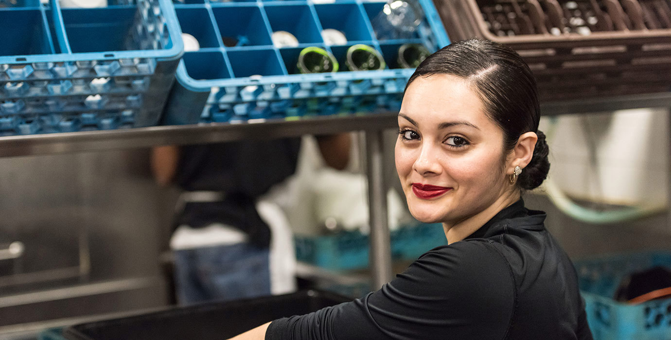 A worker puts a bin of dirty dishes on the counter in a restaurant kitchen.
