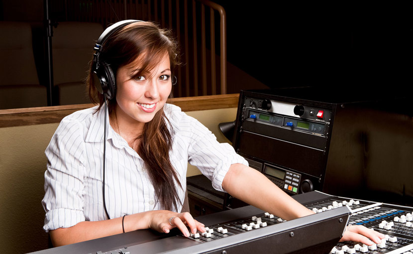 A person wearing headphones sits in front of a mixing console while smiling.