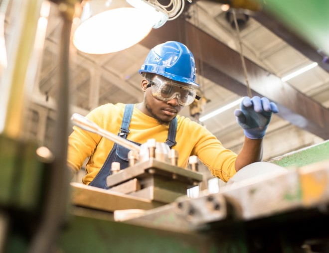 Factory engineer in hardhat and overalls using a lathe. 