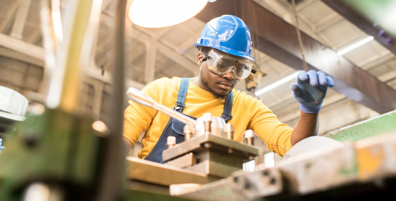 Factory engineer in hardhat and overalls using a lathe.