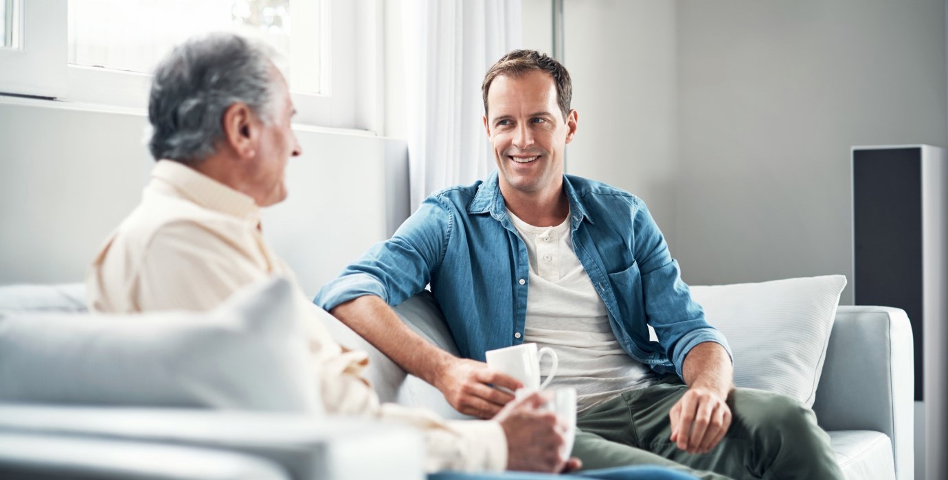 Father and son talking while sitting on couch and drinking coffee.
