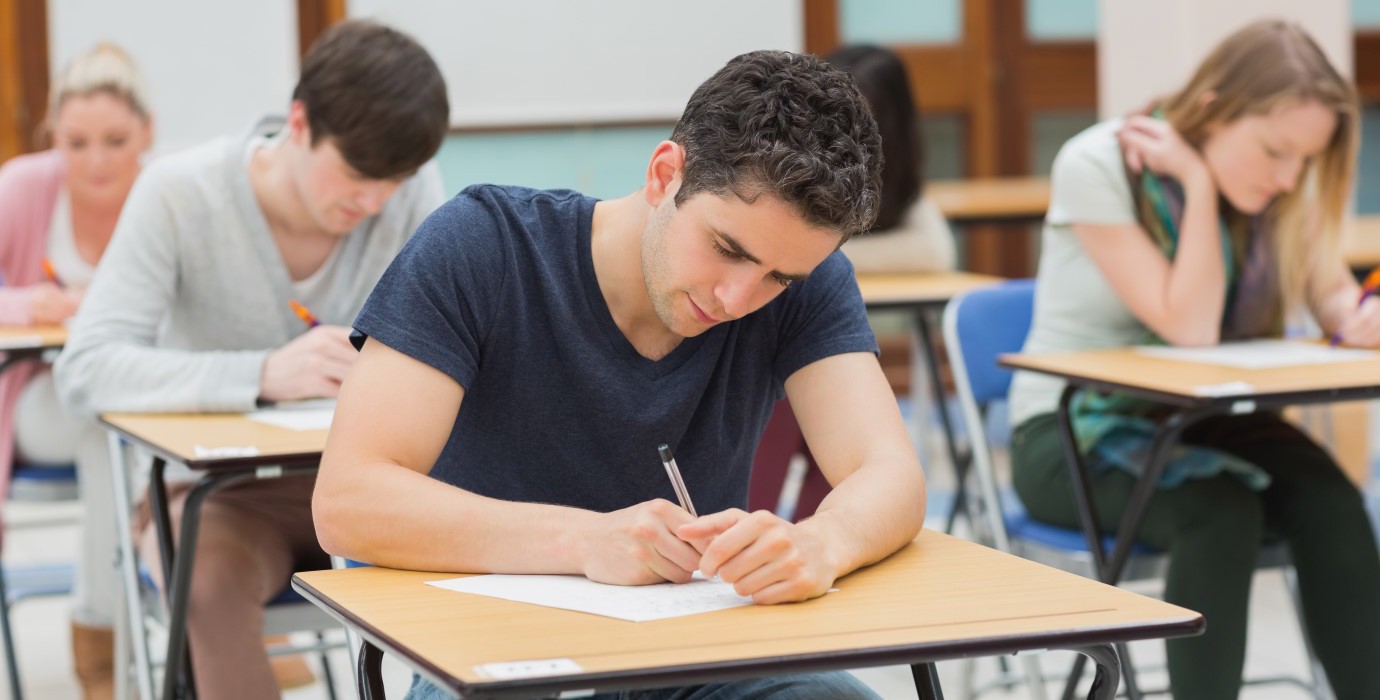 Post-secondary student writing exam at desk in a classroom.