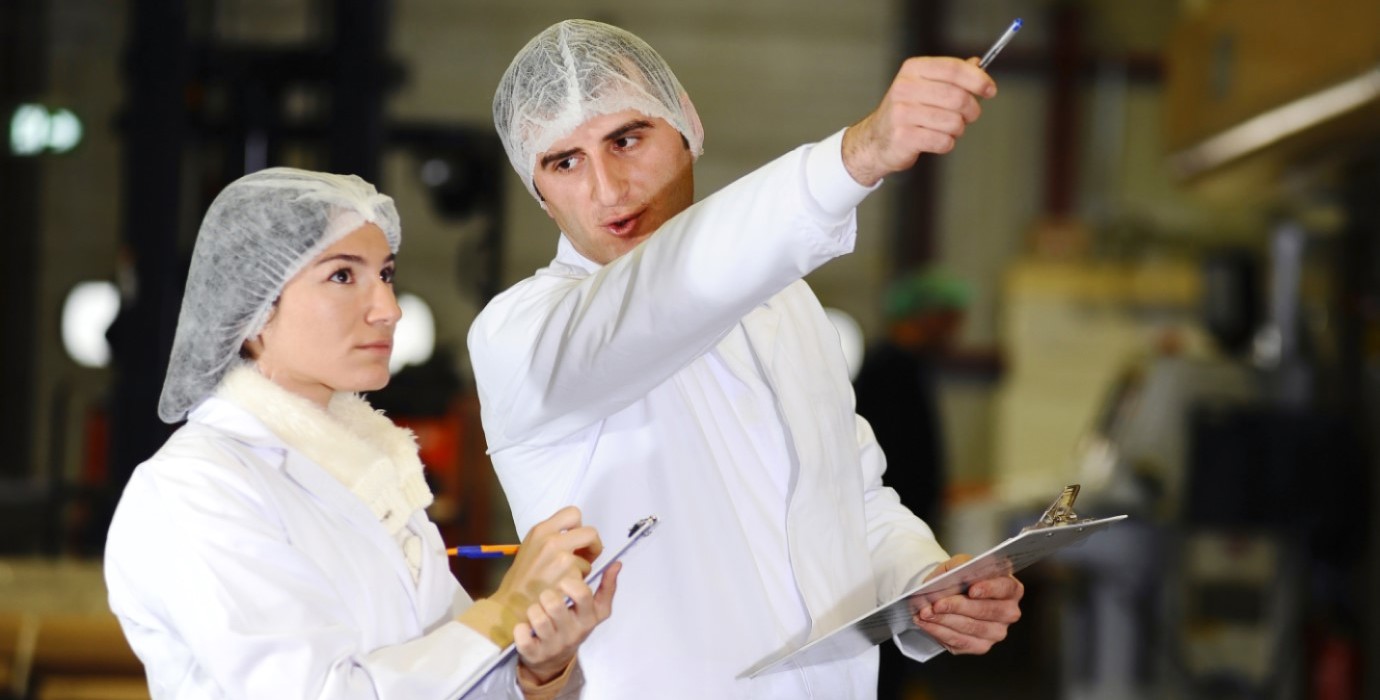 Two workers in hairnets and lab coats inspecting equipment.