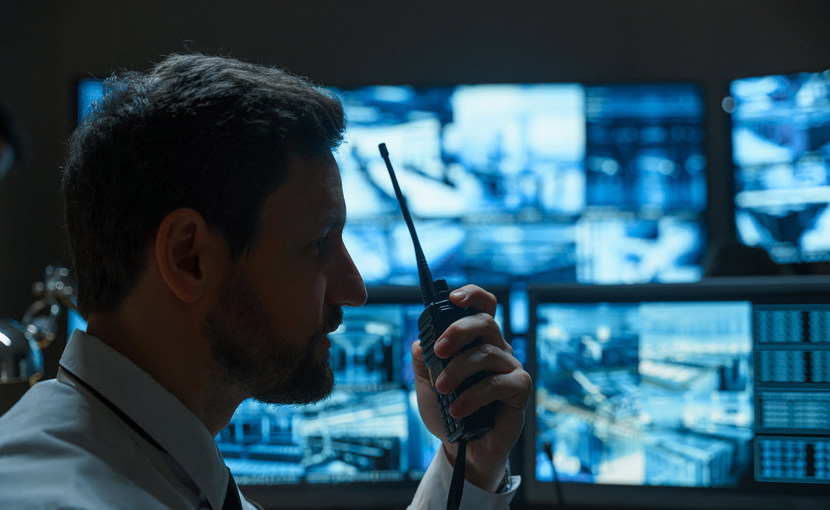 Security guard holding a walkie talkie in front of monitors