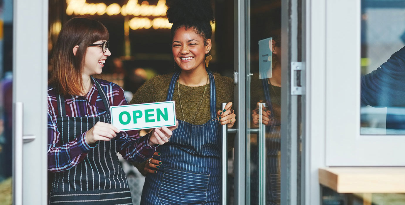 People holding an "Open" sign in front of their cafe