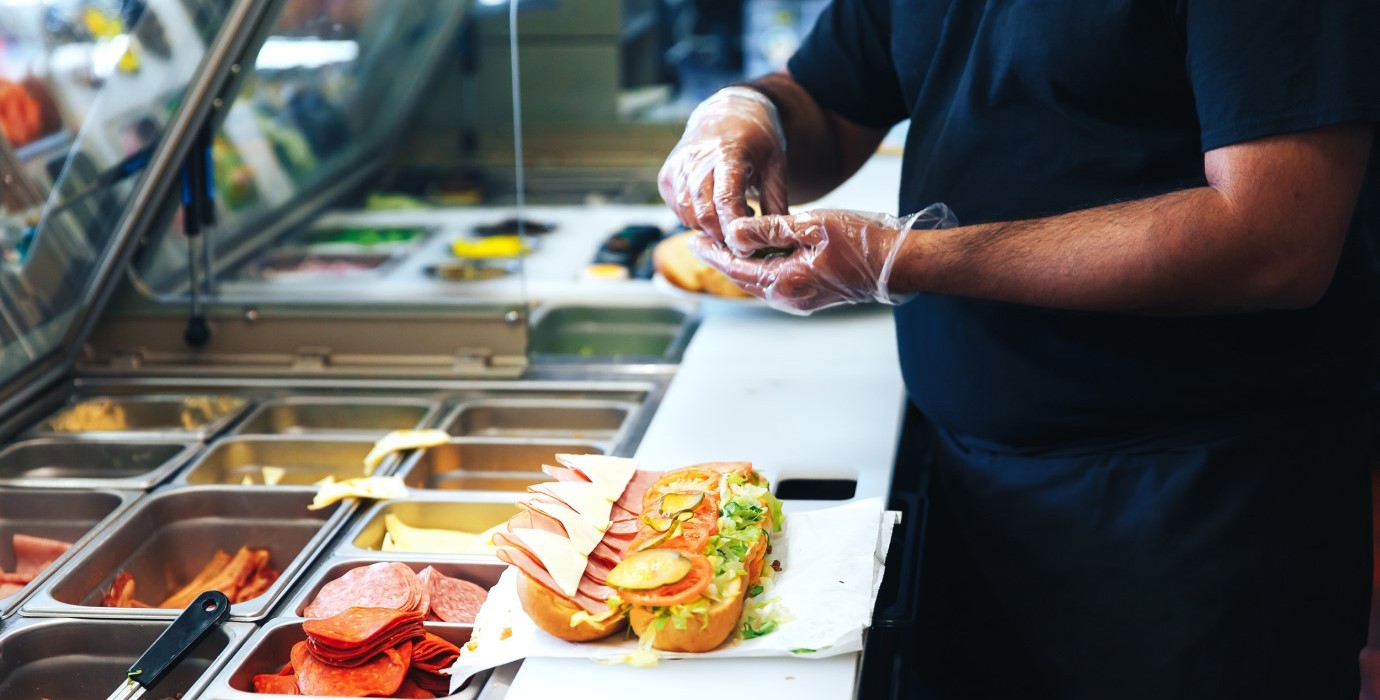 Person making a sandwich in a commercial kitchen.