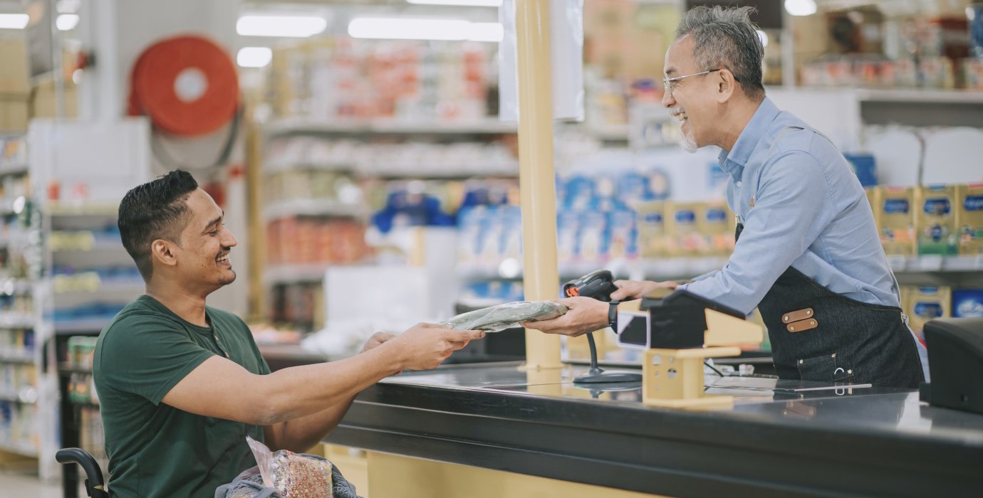 Person in wheelchair paying for groceries at checkout.
