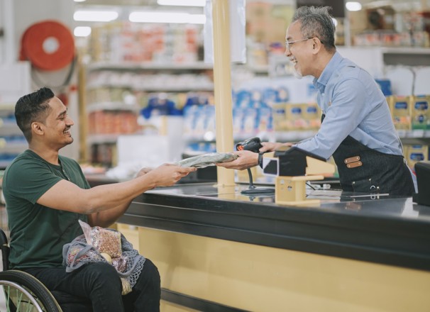 Person in wheelchair paying for groceries at checkout.