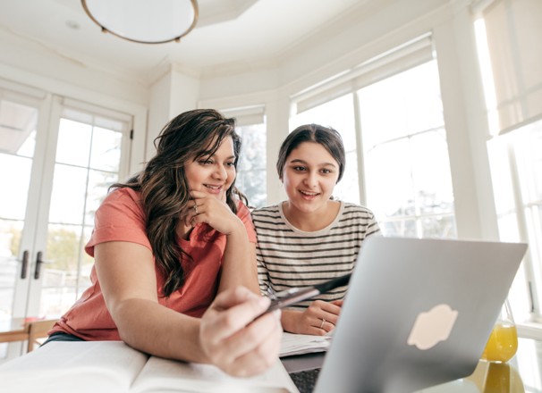 Mother pointing at laptop screen while daughter watches. 