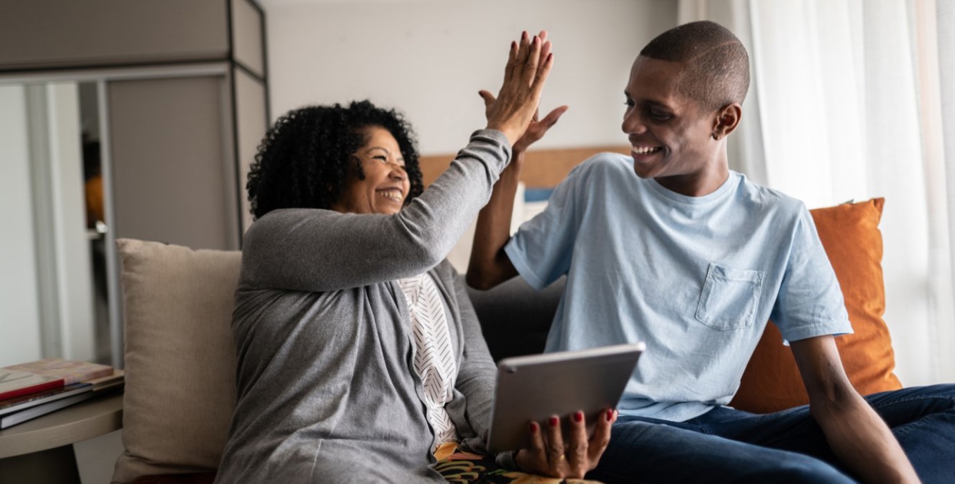 Mother high-fives her son while looking at tablet and sitting on their couch. 