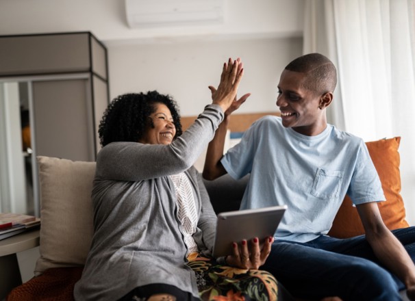 Mother high-fives her son while looking at tablet and sitting on their couch. 