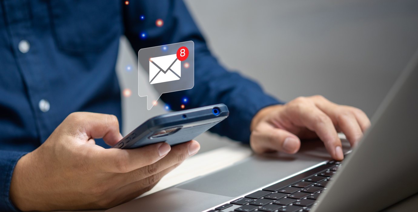 person emailing with a cellphone and a laptop